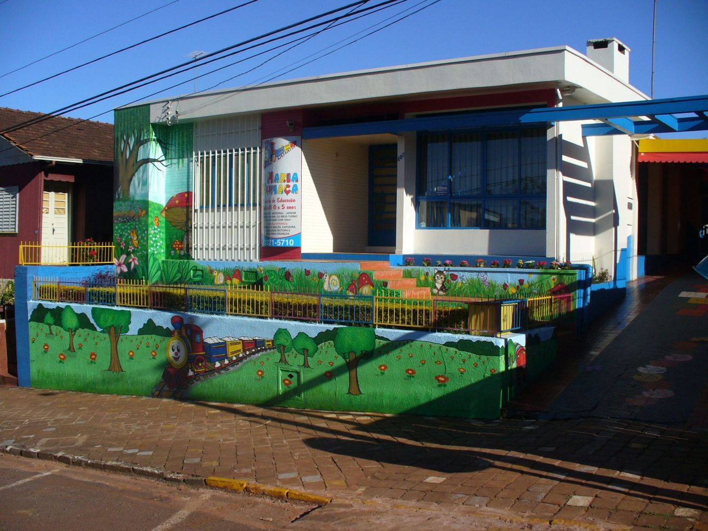 Fachada de escola com muro pintado de jardim e trem